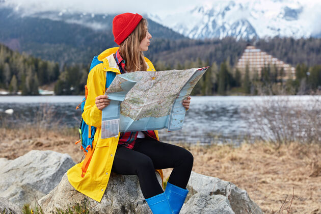人类严肃的女旅行者带着背包探索新的目的地 坐在石头上看地图 寻找一些地方地图山自然