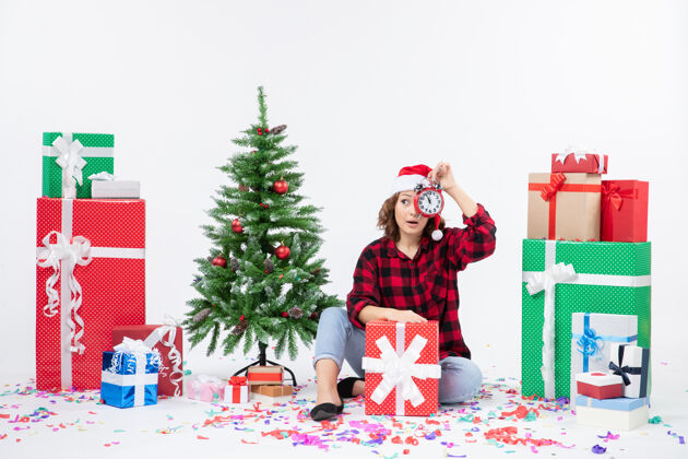 庆祝前视图的年轻女子坐在圣诞礼物周围拿着白色墙上的时钟坐着礼物礼物