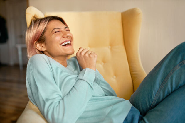 家情绪激动的欧洲年轻女子穿着牛仔裤和蓝色运动衫躺在扶手椅上闭着眼睛现代笑周末