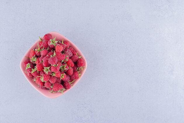 碗大理石背景上粉红色碗里的一堆覆盆子果汁美味健康