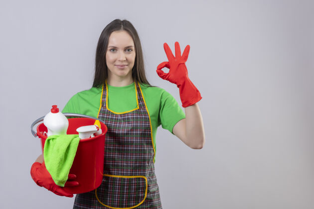好的一个穿着制服 戴着红手套 拿着清洁工具的年轻女孩 在孤立的白色背景上做了一个很好的手势高兴拿着手套
