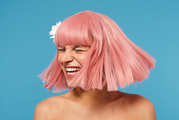 洋甘菊可爱可爱的年轻女士 粉色短发 在蓝色背景下摆着姿势 开心地笑着 头发上插着一朵白花眼影高兴花