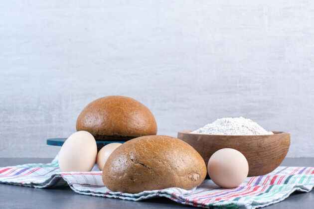 碗面粉碗 鸡蛋和面包放在大理石上的毛巾上烘焙饭馒头