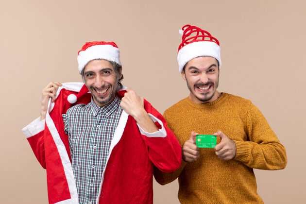 圣诞老人前视图两个快乐的家伙一个穿着圣诞老人的外套 另一个在米色的背景上有信用卡伙计们米色快乐