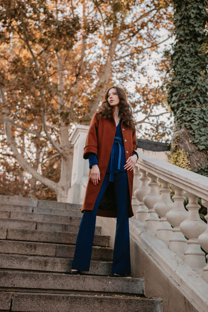 女孩美丽时尚的微笑瘦身女子卷发走在街头楼梯上穿着温暖的棕色外套和蓝色西装 秋季时尚街头风女人漂亮深色