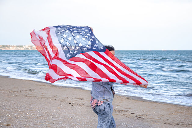 女人一位手持美国国旗的年轻女子在海边奔跑爱国主义和独立日庆祝活动的概念风文化独立日