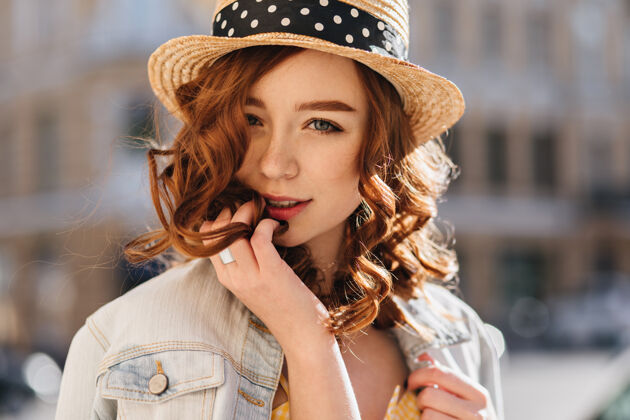 欧洲戴着帽子的漂亮白人妇女在街上摆姿势的特写照片穿着牛仔夹克的姜汁女孩的户外照片人魅力姜