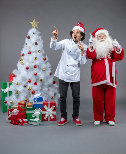 圣诞快乐圣诞老人和男厨师在灰色墙上围着圣诞礼物的正视图圣诞老人服装男性