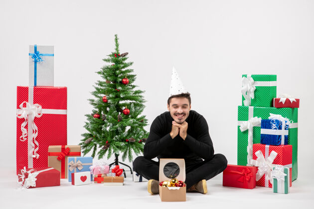 礼物年轻人坐在白色墙上的节日礼物周围的正面视图人们快乐节日