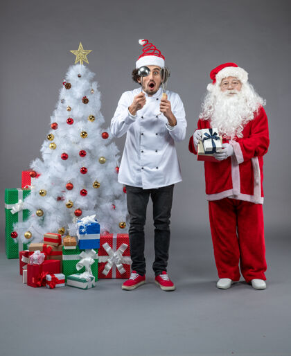 圣诞老人圣诞老人和男厨师在灰色墙上围着圣诞礼物的正视图圣诞老人厨师十二月