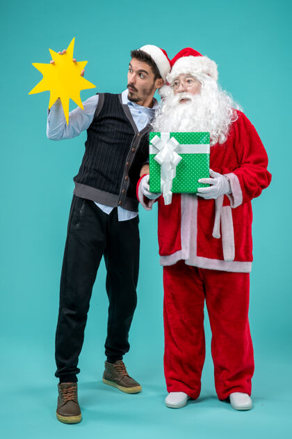 男性前视图圣诞老人与年轻男子谁持有蓝色地板上的黄色标志圣诞老人新年假期雪圣诞老人风景情侣