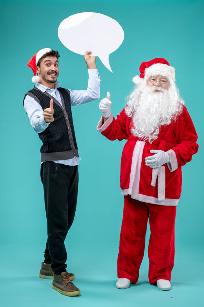 圣诞老人前视图圣诞老人与年轻的男性谁持有白色标志的蓝色背景成人圣诞老人前面