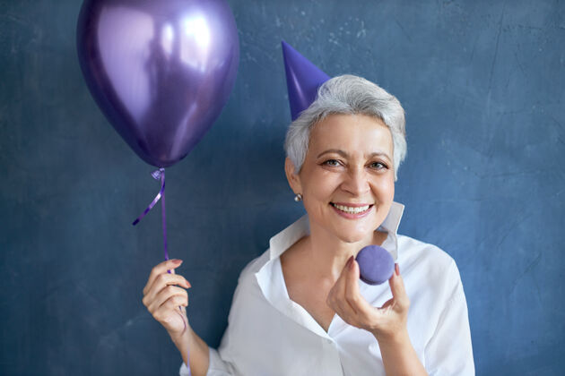 庆祝一幅孤立的肖像画 画中穿着白衬衫 手持氦气球 面带微笑的快乐放松的成熟女人甜点老年人气球