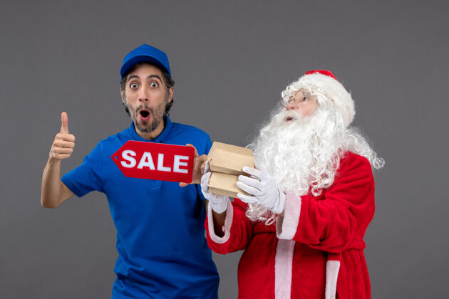 包裹圣诞老人的正面图 男信使手持销售横幅 灰色墙上有食品包装销售快递圣诞老人