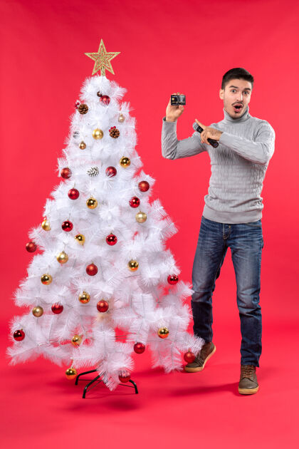 电话圣诞节心情自信的家伙穿着牛仔裤站在装饰圣诞树附近 拿着麦克风指着他的手机麦克风圣诞人