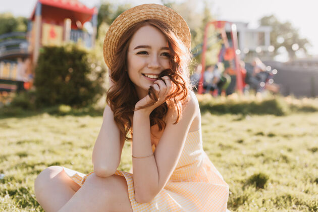 户外在阳光明媚的日子里 优雅的白人女孩坐在草地上在夏天 姜黄色卷发的年轻女士在草坪上摆姿势大笑成人草坪时尚