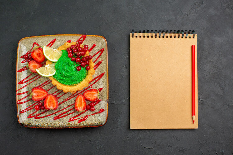 箱子顶视图美味的蛋糕与绿色奶油和草莓在黑暗的背景甜点甜茶茶信封容器