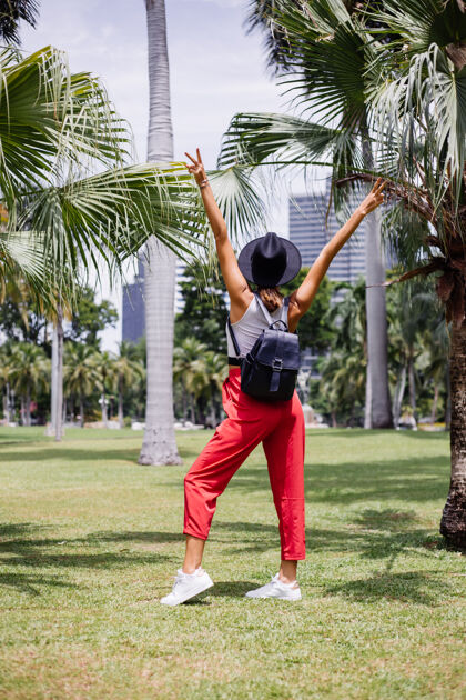 平静快乐女人背着背包环游曼谷 在绿草如茵的热带公园里享受美丽的晴天移动户外树叶