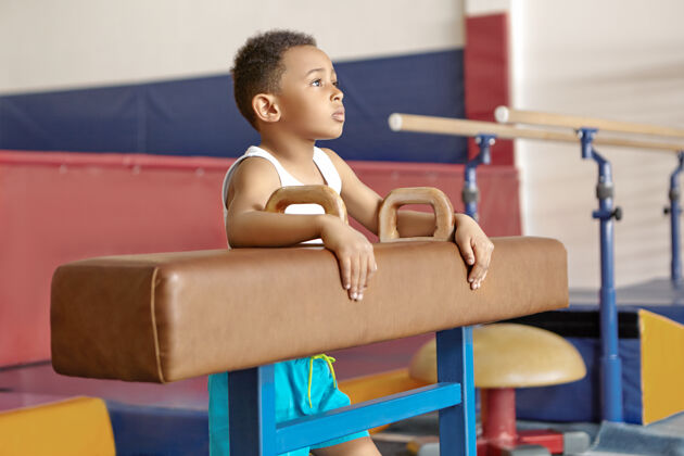体操运动员一张十岁的美国黑人小孩穿着白色t恤站在体育馆的鞍马旁的照片体操大厅年轻人