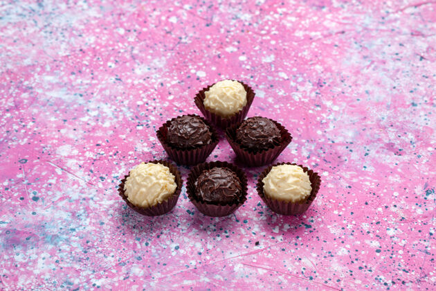 甜味前视图美味的巧克力糖果白色和黑色巧克力粉红色背景接近邦邦糖果