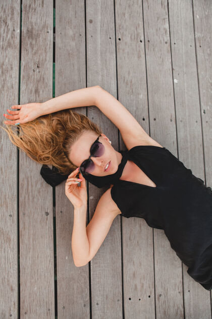 模特奢华性感迷人的女人穿着黑色连衣裙躺在地上戴着墨镜 暑假 俯瞰女人户外夏天