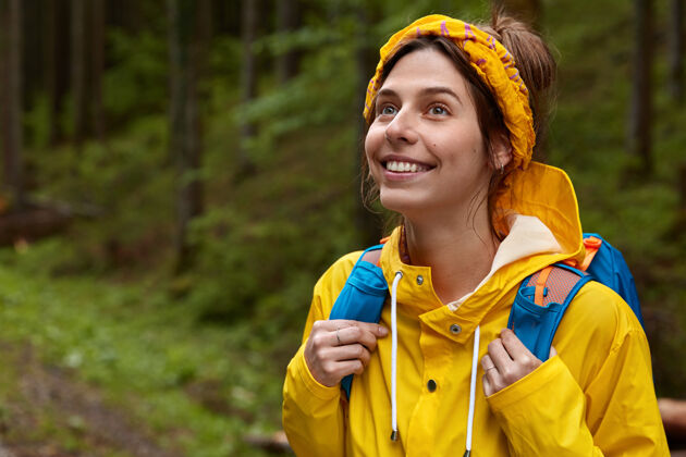 步行开朗少女的户外镜头若有所思地望向远方 戴着黄色的头巾和雨衣 在森林里漫步森林冒险享受