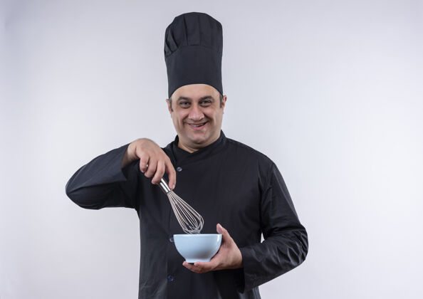 拿着微笑的中年男厨师 身着厨师制服 手里拿着搅拌器和碗厨师搅拌碗