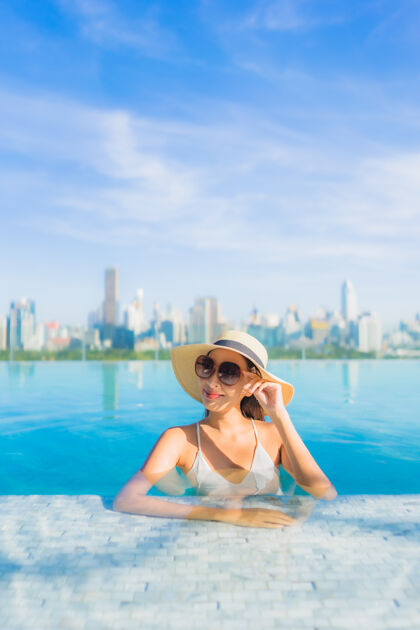 梦想肖像美丽的亚洲年轻女子微笑放松休闲围绕室外游泳池与城市景观城市现代游泳池