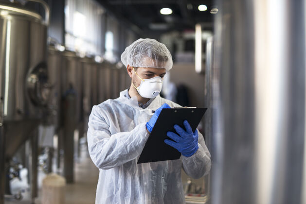 防护面罩穿着白制服的技术人员在工业生产工厂检查质量检查网络制服
