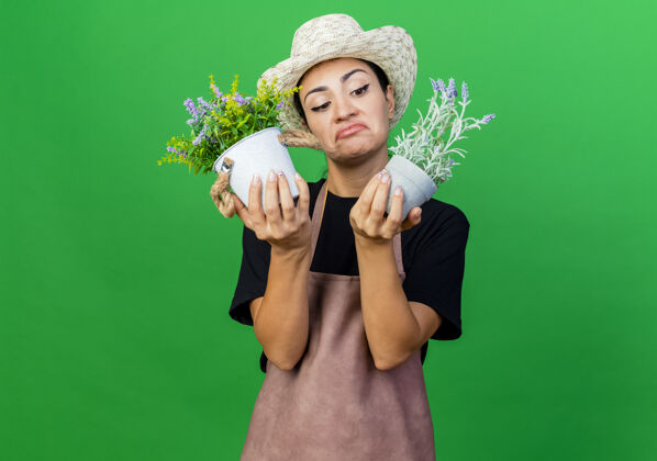 园丁年轻漂亮的女园丁 围着围裙 戴着帽子 手里拿着盆栽植物 看上去既困惑又不高兴看困惑植物