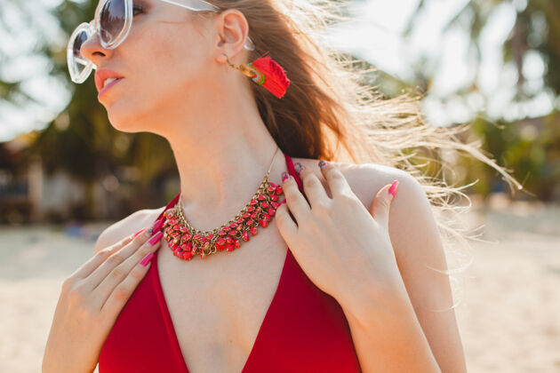 肖像年轻漂亮的金发女人穿着红色泳衣 戴着太阳镜在沙滩上晒太阳女人大海胸部