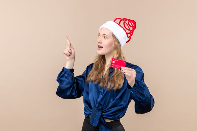 年轻女性正面图年轻女性手持粉色背景的红色银行卡度假照片新年圣诞钱情圣诞节人女士
