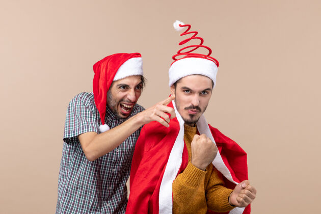 成人前视图两个圣诞节的家伙一个显示的东西 另一个在米色孤立的背景微笑米色视图