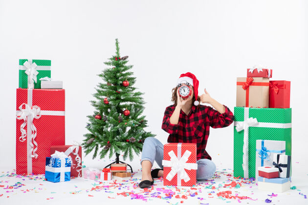 雪前视图的年轻女子坐在圣诞礼物周围拿着白色墙上的时钟圣诞快乐节日快乐