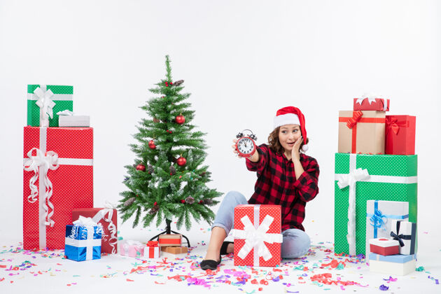 女人前视图的年轻女子坐在圣诞礼物周围拿着白色墙上的时钟快乐礼物十二月