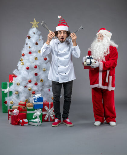 礼物圣诞老人和男厨师在灰色墙上围着圣诞礼物的正视图厨师圣诞老人前面