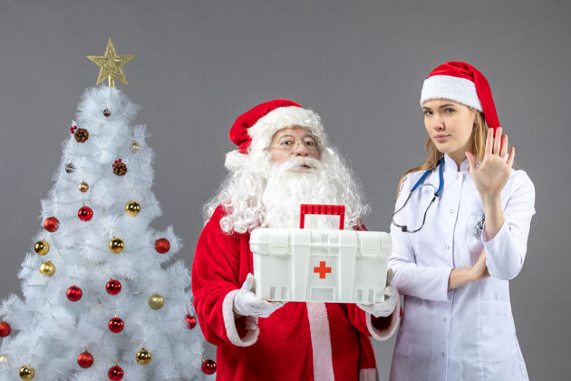 快乐圣诞老人和给他急救箱的女医生在灰色墙上的正视图人们健康人