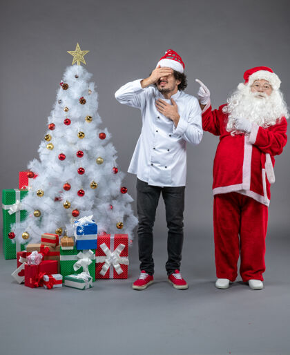 快乐圣诞老人和男厨师在灰色墙上围着圣诞礼物的正视图礼物人们圣诞老人