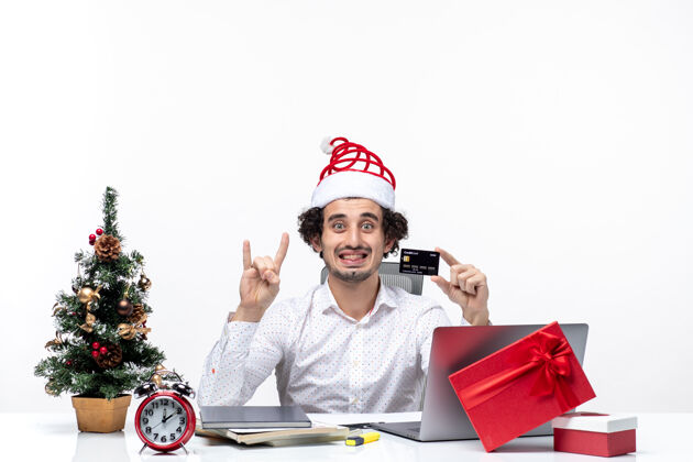 男性圣诞节心情与年轻的胡须微笑的商人与圣诞老人帽子举行银行卡和显示两个白色背景控股帽子人