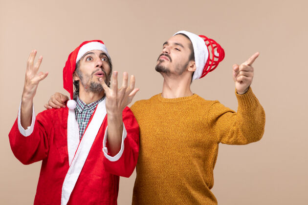 男人正面图两个戴着圣诞帽的自信男人站在米色孤立的背景上成人自信开朗