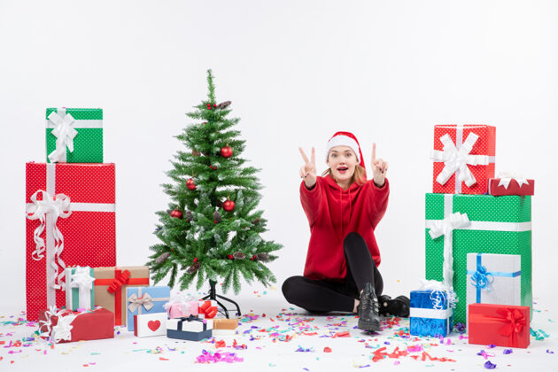 人年轻女子坐在白色墙壁上的节日礼物周围的正面视图圣诞快乐快乐寒冷