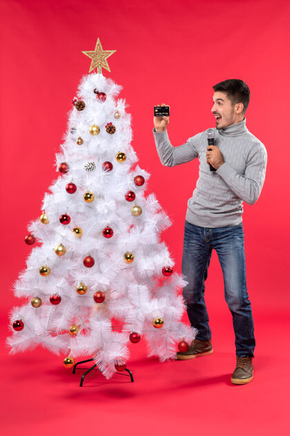 麦克风圣诞节心情自信的家伙站在装饰好的圣诞树旁 拿着麦克风拍照 开心地看着自信的家伙看着快乐