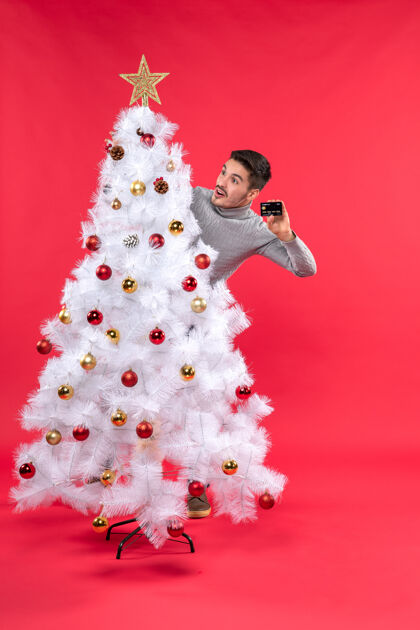 心情圣诞气氛 情绪激动的家伙站在装饰好的圣诞树后面 看起来很惊讶圣诞树礼物站着