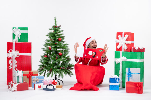 礼物圣诞老人坐在地上 在礼物旁边展示圣诞袜 白色背景上装饰圣诞树 营造出喜庆的节日气氛袜子圣诞坐