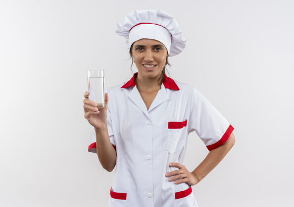 厨师面带微笑的年轻女厨师穿着厨师制服拿着一杯水把手放在臀部和复印空间女穿手