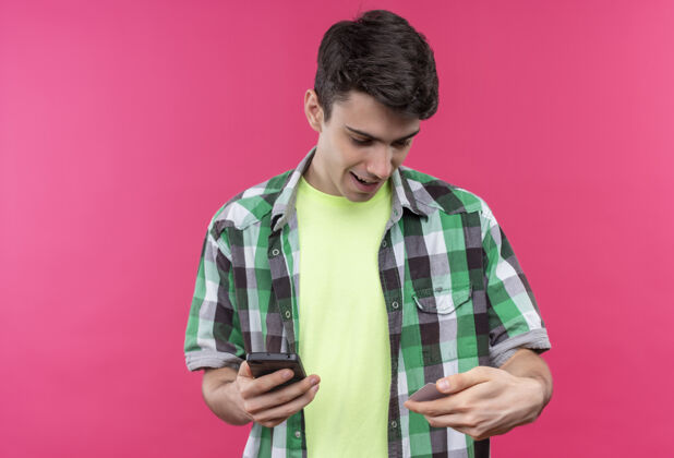 粉色微笑着的白人年轻人穿着绿色衬衫拿着电话 在孤立的粉色背景下看着手上的信用卡绿色信用卡戴着