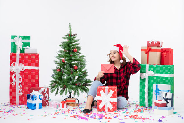 庆祝前视图年轻女子坐在周围的礼物举行信封上的白墙圣诞圣诞快乐礼物
