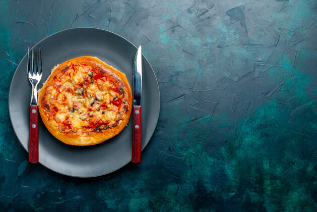 番茄小奶酪比萨饼圆的俯视图 深蓝色表面上有餐具晚餐生的成型的