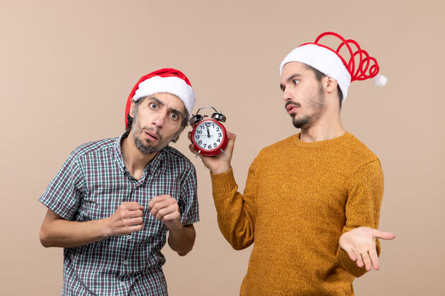 男人正面图两个男人一个在听 另一个拿着闹钟 背景是米色的帽子前面两个