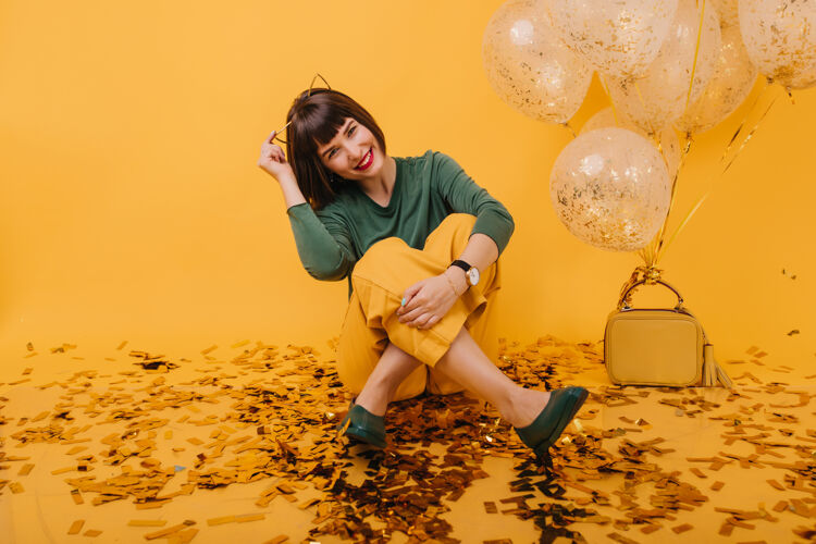 黄色快乐的女模特坐在满是五彩纸屑和欢笑的地板上迷人的高加索女孩在她的生日与气球合影欢笑快乐微笑